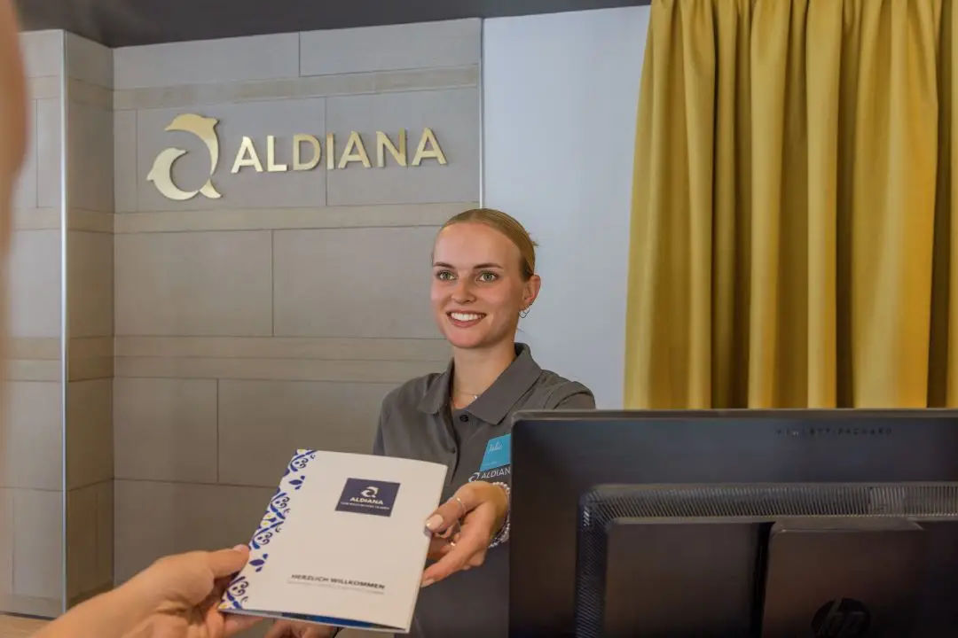 Front Office Hotel, Hotelrezeption, Frau übergibt Hotelinformationen am Empfang an Gast